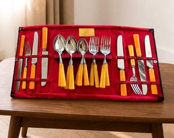 Könnte beinhalten: Ein Besteckset aus Edelstahl mit leuchtend orangefarbenen Griffen, angeordnet in einer roten Filzrolle. Das Set enthält verschiedene Messer, Gabeln und Löffel, die alle in einzelnen Fächern innerhalb des roten Stoffhalters befestigt sind.