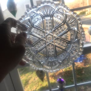 Puede incluir: Un cuenco de vidrio transparente con un patr&oacute;n decorativo intrincado. El cuenco tiene un borde festoneado y un dise&ntilde;o central elevado.