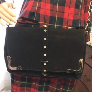 May include: A black suede handbag with a gold chain strap and a silver buckle closure. The bag has a row of rhinestones down the center.