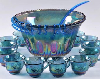 May include: A large iridescent blue glass punch bowl set featuring a scalloped rim, a matching blue ladle, and twelve small glass cups. The bowl and cups display a textured floral pattern with a reflective, multi-colored metallic sheen.