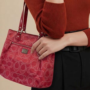 May include: A red handbag featuring a repeating white C-logo pattern, a front zippered pocket, and glossy red shoulder straps. The bag includes a rectangular metal brand plaque on the front and silver-toned hardware accents throughout the design.