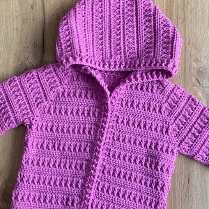 May include: A purple crocheted cardigan with a hood. The cardigan has a front zipper and a ribbed texture.
