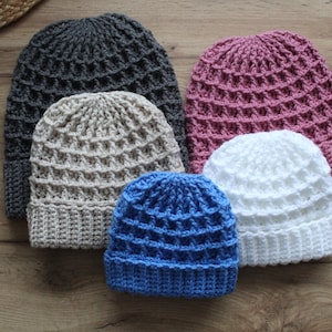 May include: Five crocheted hats in different colours, including grey, beige, pink, white, and blue. The hats are all made with a waffle stitch pattern.