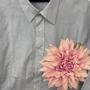 Könnte beinhalten: Ein Hemd mit dünnen, vertikalen blauen Streifen auf weißem Grund. Das Hemd hat einen klassischen Kragen und ist teilweise geknöpft. Eine große, rosa-pfirsichfarbene Blume liegt auf dem Hemd. Das Etikett lautet "Made by Flensboms for Austin Reed Royal Crest."