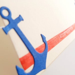 Peut inclure: Une ancre bleue avec une bande rouge en haut. L'ancre est en papier et a une surface textur&eacute;e.