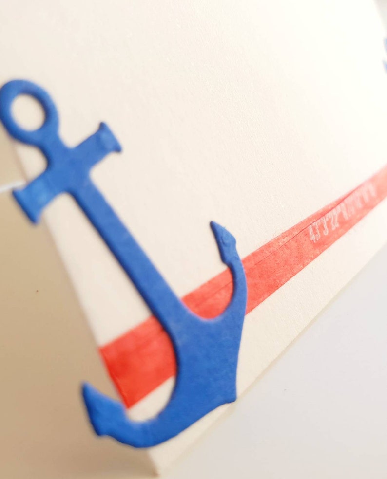 Peut inclure: Une ancre bleue avec une bande rouge en haut. L'ancre est en papier et a une surface textur&eacute;e.