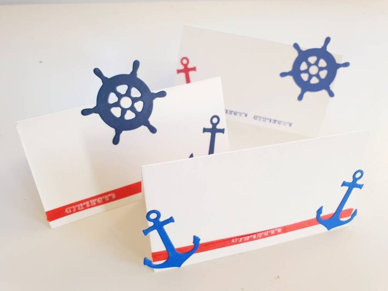 Peut inclure: Quatre cartes de place blanches avec des d&eacute;corations nautiques rouges et bleues. Les d&eacute;corations comprennent des ancres et des volants. Les cartes de place ont une bande rouge avec le mot "Strawberry" imprim&eacute; dessus.