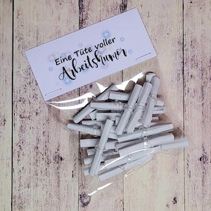 May include: A white bag with a white card that says "Eine Tüte voller Arbeitshumor" and contains rolled up white pieces of paper.