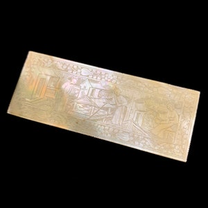 Puede incluir: Una pieza rectangular de nácar con un diseño intrincado de personas y edificios. El diseño está tallado en la superficie de la perla y es muy detallado.