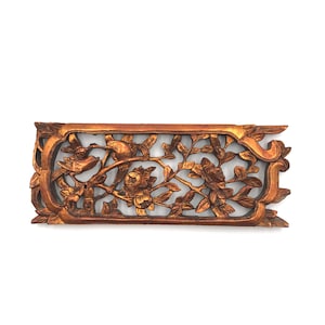 May include: A carved wooden wall panel with a floral design and birds. The panel is painted in shades of gold and brown.