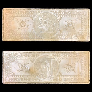 Puede incluir: Dos paneles rectangulares de nácar con intrincados diseños florales y escenas grabadas. El panel superior presenta un león sosteniendo un hacha, mientras que el panel inferior representa a una persona sosteniendo un cubo.