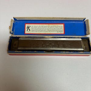 May include: Vintage Hohner harmonica in its original box. The box is blue with a red and white interior. The harmonica is silver with the brand name "M. Hohner" visible. The box has text that reads "M. Hohner".