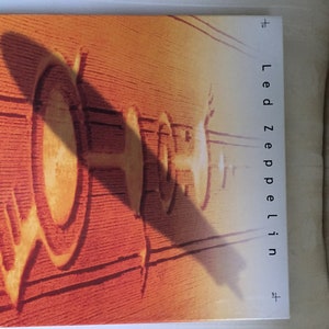 May include: Led Zeppelin album cover featuring a wooden door with carved details and the band's name in white. The cover has a warm, orange and brown color palette, with shadows adding depth.