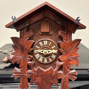 Traditional hand carved wooden Black Forest cuckoo clock with vine and leaf motif, made in Germany.