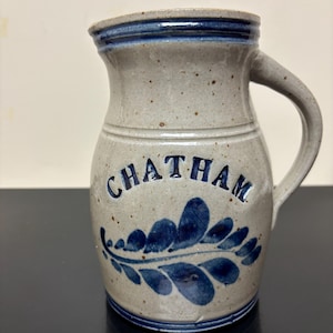 May include: A stoneware pitcher with a light gray speckled finish. The word "CHATHAM" is printed in blue, along with a blue leaf design. The rim and a band around the neck are also blue.