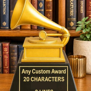 May include: A gold-colored gramophone trophy featuring a black base with a plaque that reads Any Custom Award 20 CHARACTERS 3 LINES. The award has a square base, a circular turntable, and a large, curved horn extending from the top of the structure.