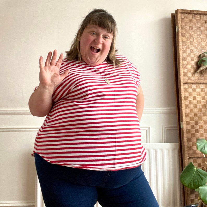 May include: A woman wearing a red and white striped shirt with a short sleeve and a scoop neck. She is also wearing dark blue jeans.