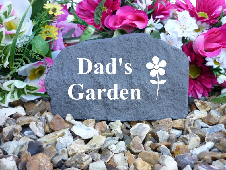 May include: A gray stone garden marker with the text "Dad's Garden" and a white flower design.
