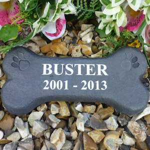 May include: Black bone-shaped pet memorial stone with the name "Buster" and the dates "2001 - 2013" engraved in white.