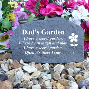 May include: A gray stone garden memorial with the text "Dad's Garden" and a poem about a secret garden. The stone is surrounded by small pebbles.