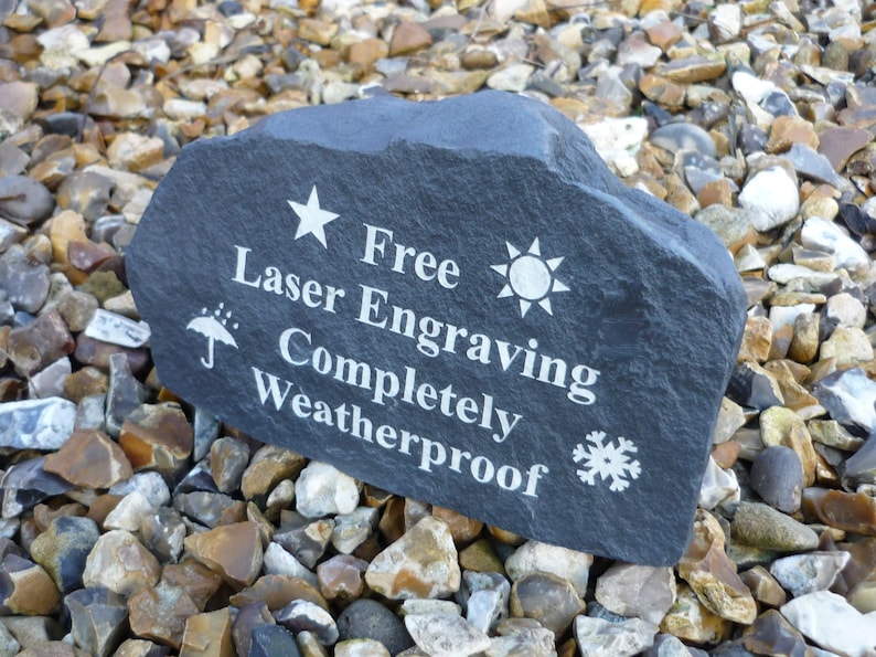 May include: A black slate rock with white text that reads "Free Laser Engraving Completely Weatherproof". The text is surrounded by symbols including a star, sun, snowflake, and umbrella.