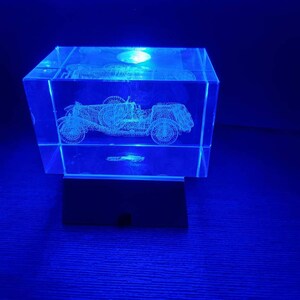 May include: A crystal cube with a 3D laser-engraved image of a vintage car. The cube is illuminated from the bottom with a blue light.
