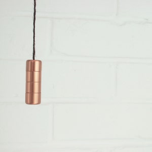 Może przedstawiać: Koperowy włącznik światła z czarnym kablem wiszący na białej ceglanej ścianie.