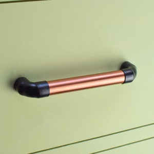 May include: A copper pipe drawer pull with black end caps. The pull is mounted on a light green surface.