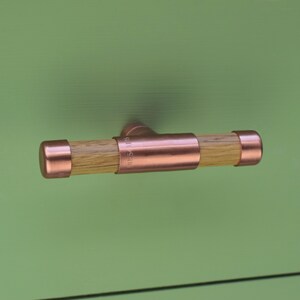 May include: Copper and wood cabinet pull with a T-shaped design. The pull has a copper finish and a wooden center section.