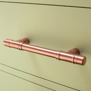 May include: A copper pipe drawer pull with a T-shaped design. The pull is made of copper pipe and has a polished finish.