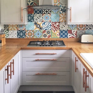 May include: A kitchen with white cabinets and a wood countertop. The backsplash is a colorful mosaic of tiles. The stovetop is stainless steel with four burners. The cabinets have copper handles.