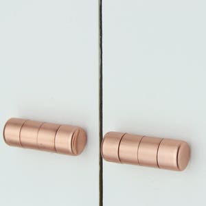 Op de afbeelding: Twee rozégouden kastdeurgrepen, elk gemaakt van vier gestapelde cilinders.