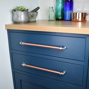 May include: Two drawers with copper pipe handles on a dark blue cabinet. The handles have a polished chrome finish.