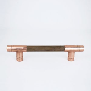 May include: A copper and wood cabinet pull with a dark wood centre and copper end caps. The end caps have the text "ENDURA" engraved on them.