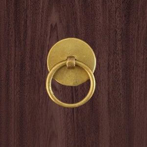 Könnte beinhalten: Ein runder Türgriff aus Messing mit einem runden Sockel. Der Griff ist eine einfache Ringform und ist an einem runden Sockel befestigt.