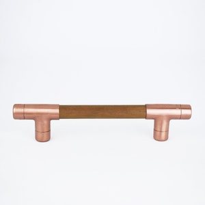 May include: A copper and wood cabinet pull with a T-shaped design. The pull is made of a solid wood bar with copper end caps.
