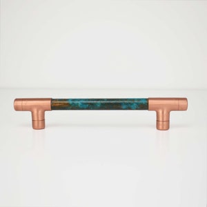 May include: A copper and turquoise blue cabinet pull with a t-shaped design. The pull is made of metal and has a rustic finish.