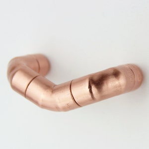 May include: A copper pipe handle with a 90-degree bend. The handle is made of multiple sections of pipe that are joined together.