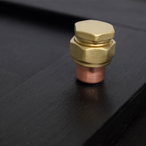May include: A gold-colored metal pipe fitting with a hexagonal cap. The fitting is on a black surface.