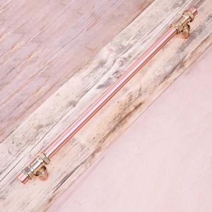 May include: A copper pipe door handle with brass fittings. The handle is mounted on a wooden surface.