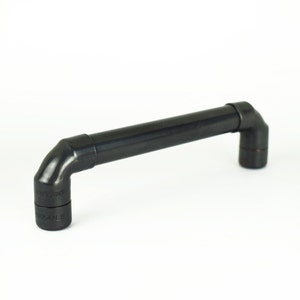 May include: Black metal pipe style cabinet door pull with a 90-degree bend on each end. The pull is approximately 6 inches long.