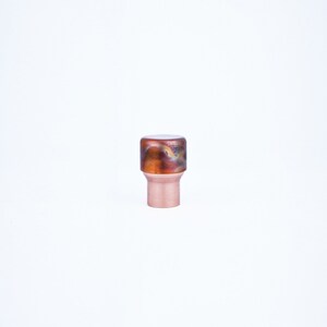 Könnte beinhalten: Ein Schrankknopf aus Kupfer und braunem Harz mit einem Wirbelmuster.