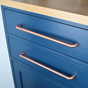 May include: Two drawers with copper pipe handles on a dark blue cabinet. The cabinet is made of wood and has a light wood top.