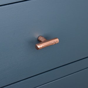 May include: A copper T-shaped drawer pull on a dark blue cabinet.