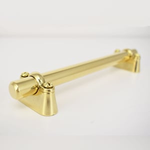 May include: A polished brass door handle with a cylindrical design and two mounting brackets. The handle is smooth and has a shiny finish.