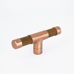 May include: A copper T-shaped cabinet pull with a wooden bar. The pull has a smooth, polished finish.