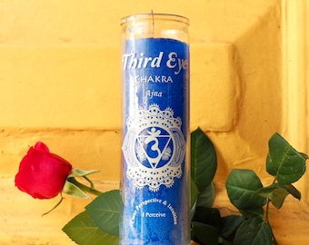 May include: Blue candle with a white label that says "Third Eye Chakra Ajna Clear Perspective & Intuition I Perceive". The label also has a white symbol with a circle around it.