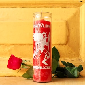 Puede incluir: Vela roja de vidrio con una imagen blanca de un diablo corriendo y el texto "Run Devil Run" y "Corre Diablo Corre".