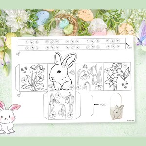 May include: A printable Easter bunny gift box template. The box is made up of six panels, each with a different design. The front panel features a bunny face, while the other panels feature flowers, bees, and butterflies. The template includes instructions for folding and assembling the box. "FOLD" is written on the template.