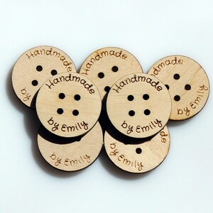 May include: A close-up of six round wooden buttons with the text "Handmade by Emily" engraved on each button.